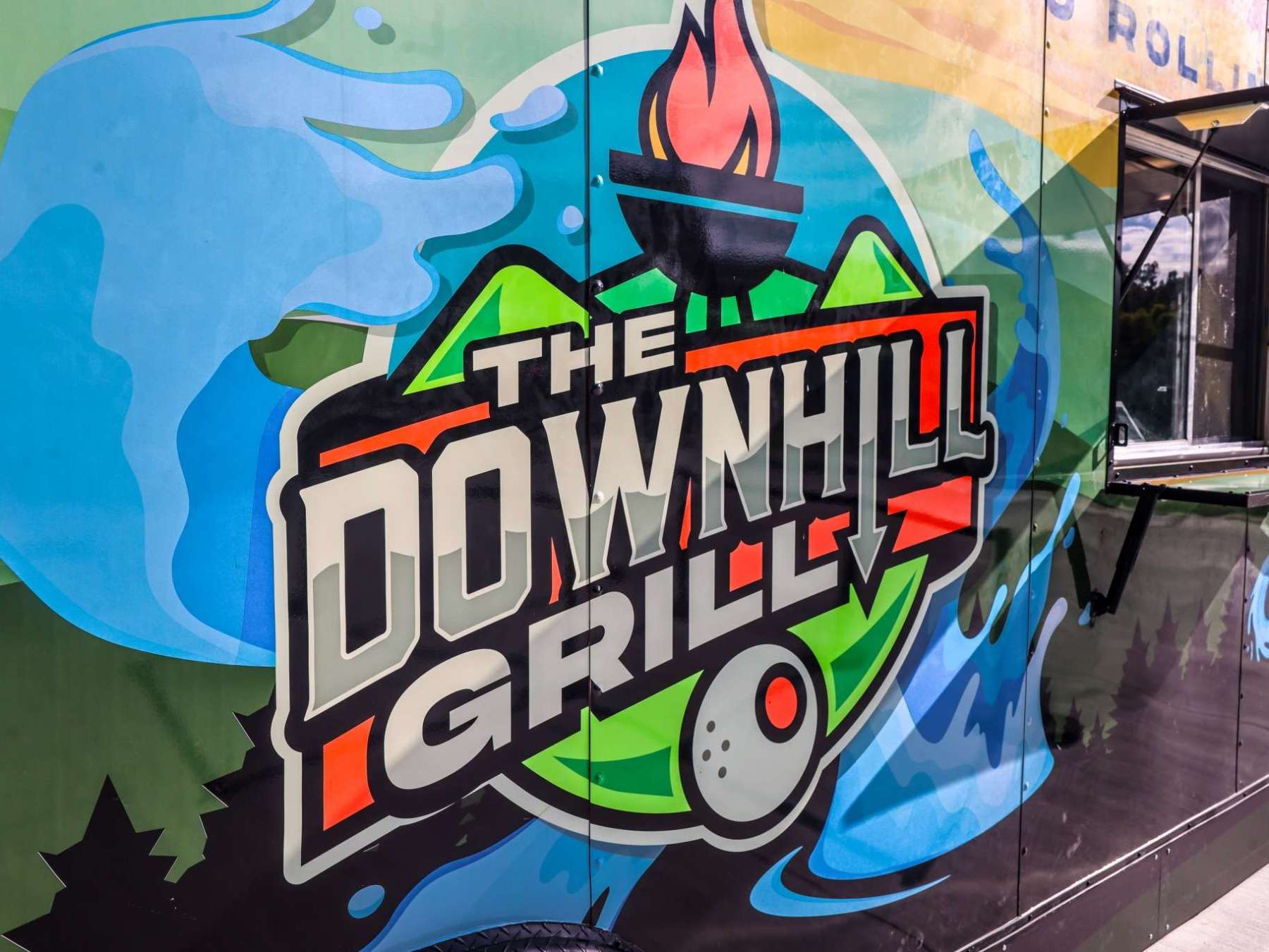 Colorful food truck with 'The Downhill Grille' logo and open service window.