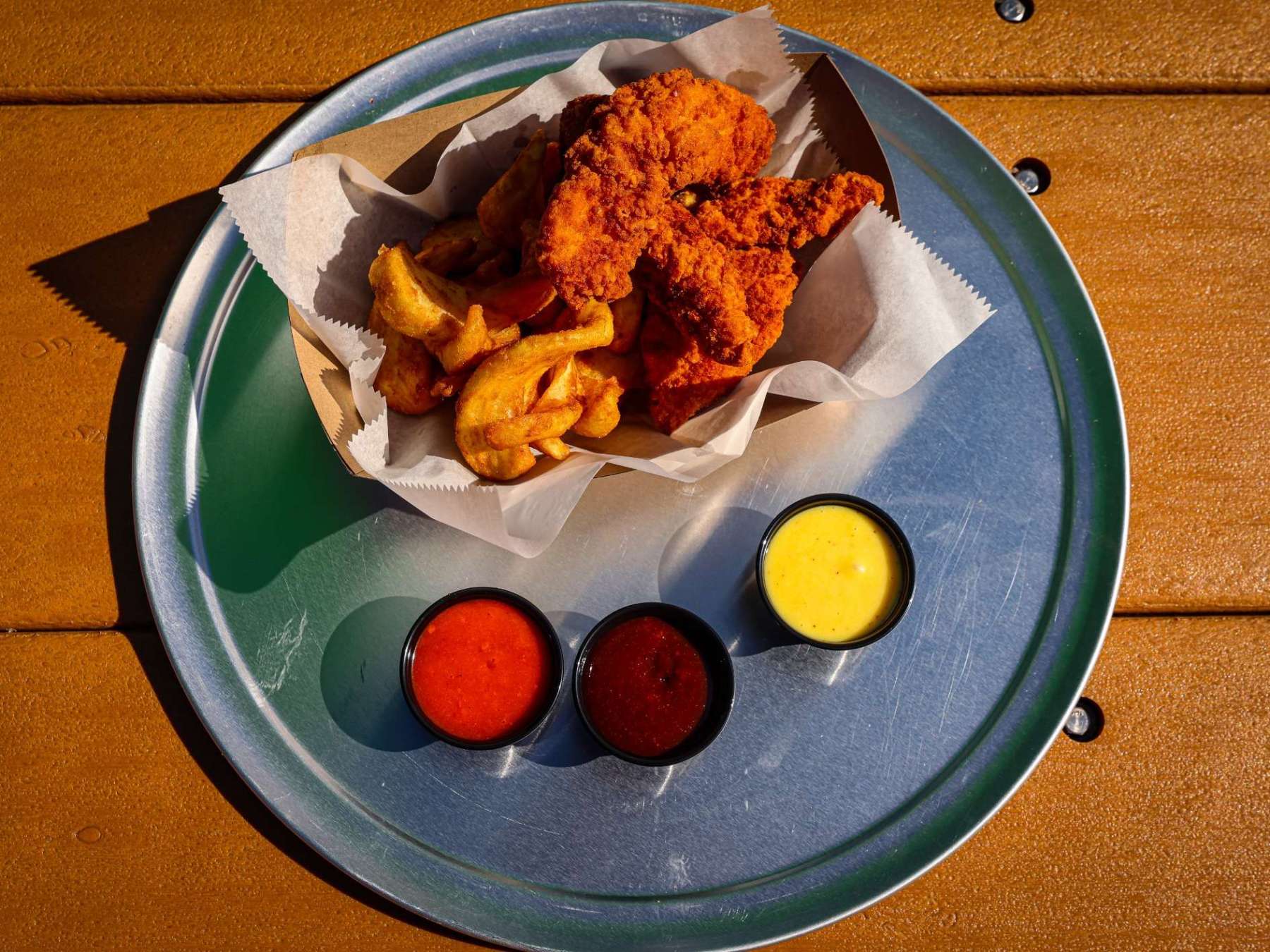 Fried chicken and fries with three dipping sauces on a metal tray.